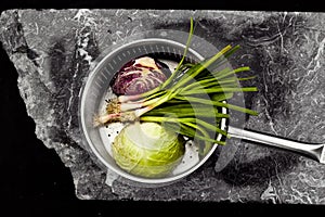 Aerial photo of a saucepan with vegetables on a stone slab.