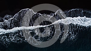 Aerial photo of waves on black sand beach.