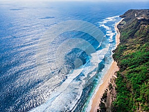 Aerial photo of a wild beach in Bali. A long strip of beach and a steep mountain slope covered with greenery. Wild beach in Bali