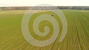 Aerial photography of a tractor spraying chemicals on a large green field, agribusiness concept