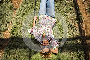 Aerial point of view for pretty woman smile and rest laying down on a timo grass. hippy and fashion clothes with jeans. sunglasses photo