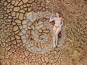 Aerial portrait of beautiful young lady in bikini lying on dry cracked red soil. arid, cracked red soil drought and arid