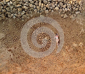 Aerial portrait of beautiful young lady in bikini lying on dry cracked red soil. arid, cracked red soil drought and arid