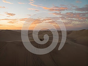 Aerial postcard panorama sunset view of buggy tour grop on dry sand dunes desert of Huacachina Ica Peru South America