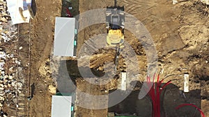 Aerial of powerful yellow excavator digging trench with bucket. Laying of underground power cables in red flexible