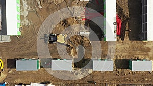 Aerial of powerful yellow excavator digging trench with bucket. Laying of underground power cables in red flexible