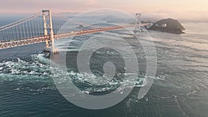 Aerial: Pullback on whirlpools under Naruto suspension bridge at sunset