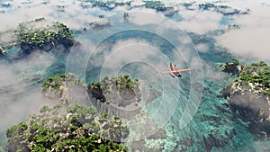 Aerial of red airplane flying over coastal landscape with rocks and trees.