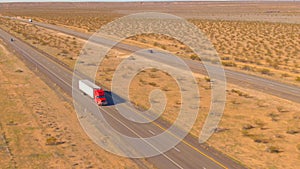 AERIAL: Red cargo truck hauls a heavy container across the barren landscape.