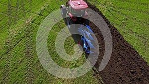 Aerial of red tractor working on green field plowing soil
