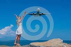 Aerial Rendezvous: Girl in White Dress on Stones, Plane Above the Blue Sea