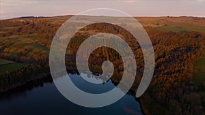 Aerial reveal of calm still lake and Reservoir at sunset over Bradfield village