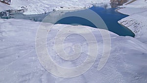 Aerial revealing shot of alpine Tilicho lake and trekkers on famous trekking trail and viewpoint surrounded by snowy