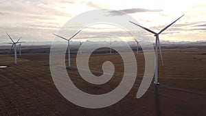 Aerial rising cinematic shot of windmills standing still on agriculture fields with Canadian Rockies