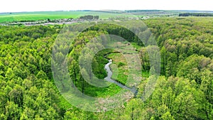 Aerial. The river flows towards the village between the green forest.