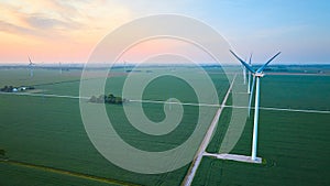 Aerial row of wind turbines in green farmland fields at sunrise or sunset with orange and pink sky