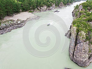 Aerial of a rubber motor boat sailing on a green river in the mountains between rocks and cliff