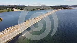 Aerial sand spit with cars parked overlooking beaches and people on summer vacation in Victoria British Columbia Canada.