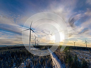 Aerial scenic photo over forest winter road with windmills standing in row at the left side in forest. Road in the middle of view