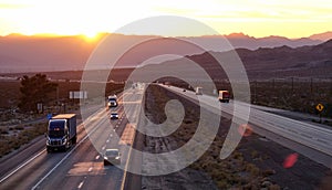 AERIAL: Scenic shot of 18 wheeler trucks and cars crossing Mojave desert at dusk