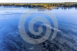 Aerial scenic view over Swedish villages and crystal clear frozen lake in Northern Scandianvia. Sun in clear sky, blue ice, winter