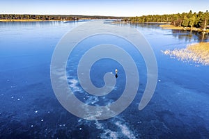 Aerial scenic view: unidentified person ice skating on crystal clear frozen lake in Northern Scandianvia. Clear skies, blue ice,