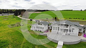 Aerial shooting of a beautiful light gray country cottage surrounded by green fields and forest on the horizon