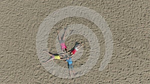 Aerial shooting of four children in bright clothes lie on sand in shape of star