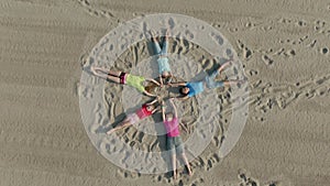 Aerial shooting of a friendly team of children in bright clothes lie on the sand