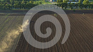 Aerial shot of agricultural field with tractor pulling a disc harrow over agricultural field, farmland