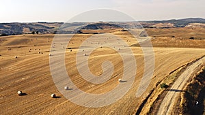 Aerial shot of agricultural fields with golden grass and rounded hays spread all over