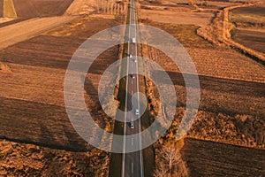 Aerial shot of autumn road through countryside landscape with cars driving away to the horizon