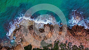 Aerial shot of a beach with crystal-clear blue water surrounded by rocks and lush green trees.