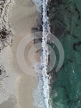 Aerial shot of a beach, featuring rocks and crystal-clear blue water