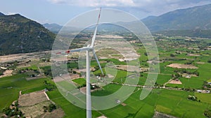 Aerial shot. A big green filed with lots of wind power plants. One power plant is under construction. Investment in