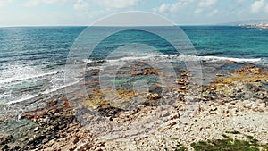 Aerial shot of blue ocean and rocky beach seashore with waves splashing against rocks. Drone view of coastline in Cyprus Paphos