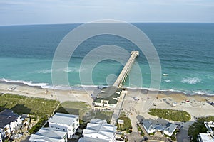 aerial shot of the blue ocean water along the coastline at Johnnie Mercer\'s Fishing Pier with homes, people on the sand
