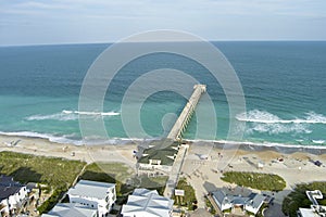 aerial shot of the blue ocean water along the coastline at Johnnie Mercer\'s Fishing Pier with homes, people on the sand