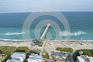 aerial shot of the blue ocean water along the coastline at Johnnie Mercer\'s Fishing Pier with homes, people on the sand