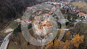 Aerial shot of Bran Castle (Dracula's Castle) surrounded by trees with a village in the background