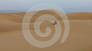 Aerial shot of buggy jeep driving between huge sand Peruvian dunes, appears.