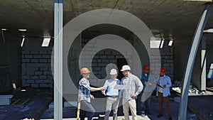 Aerial shot of builders team on construction site discussing plan of project with architect and contractor using