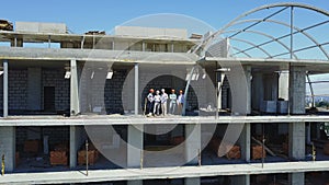 Aerial shot of builders team on construction site discussing plan of project with architect and contractor using