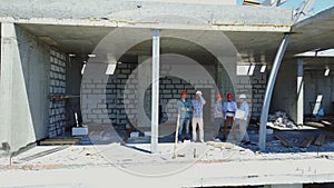 Aerial shot of builders team on construction site discussing plan of project with architect and contractor using