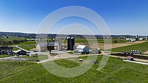 Aerial shot of busy farm complex, multiple barns silos surrounded by pastures, farm equipment in use