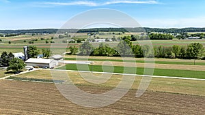 Aerial shot capturing serene beauty of rural farm, mix of plowed fields, green crops, farm buildings