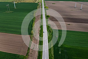 Aerial shot of car driving down the straight road through countryside landscape