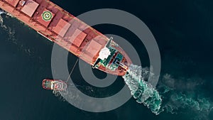 Aerial shot of a cargo ship approaching port with help of towing ship