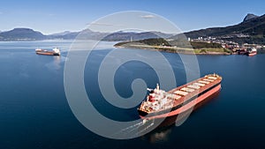 Aerial shot of a cargo ship on the open sea with other ship and mountains in the background