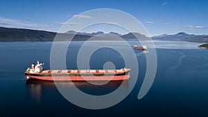 Aerial shot of a cargo ship on the open sea with other ship and mountains in the background